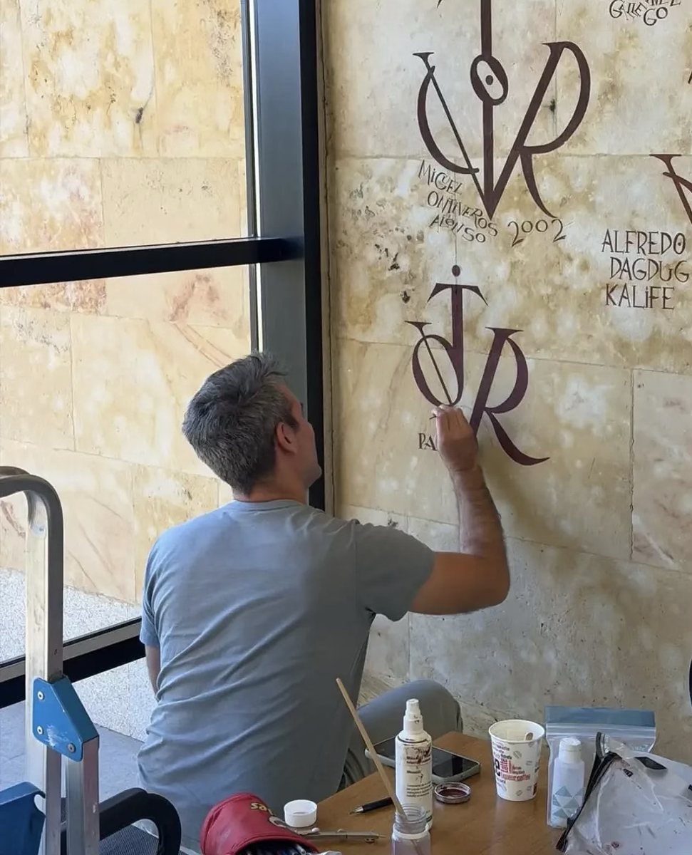 Artista pintant un vítor sobre un mur de pedra